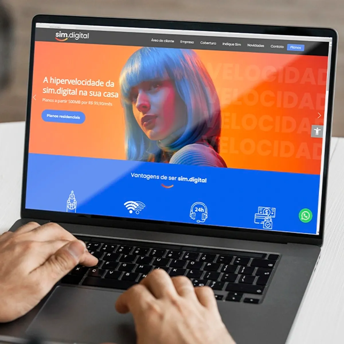 Mãos digitando em um laptop, cuja tela exibe a página inicial do site da sim.digital, cliente da W3COM. O design é vibrante, com as cores laranja e azul, destacando a 